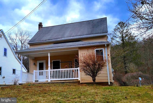 view of front of house with covered porch, a shingled roof, a chimney, and a front yard