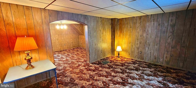 corridor featuring arched walkways, carpet flooring, wood walls, and a paneled ceiling