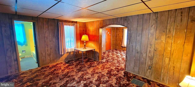 corridor with carpet floors, wood walls, visible vents, and arched walkways