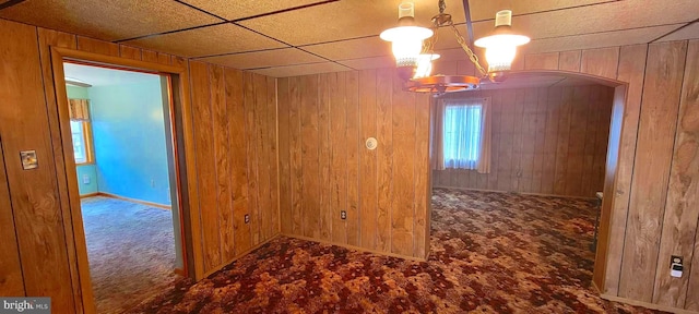 spare room featuring a notable chandelier, arched walkways, carpet flooring, and wooden walls