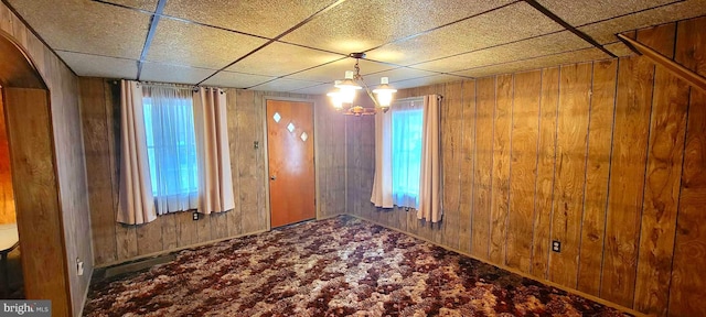 carpeted spare room with wood walls and a drop ceiling