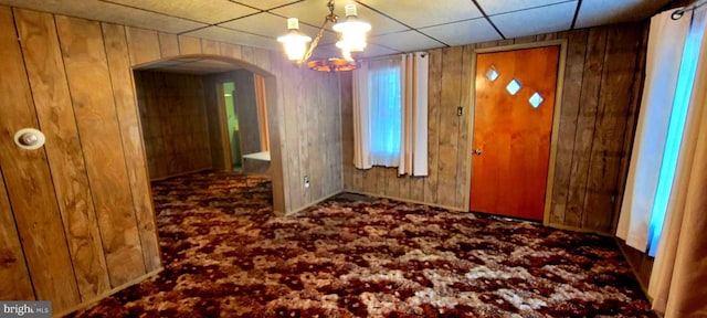 foyer featuring arched walkways, carpet flooring, and wood walls