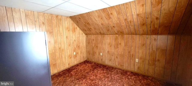 bonus room featuring lofted ceiling, wood walls, and dark colored carpet