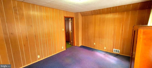 unfurnished room featuring wood walls, visible vents, and dark carpet