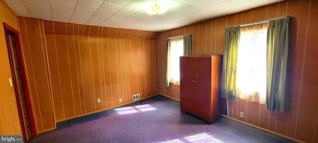 carpeted empty room with visible vents and wooden walls