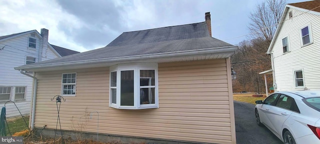 view of side of property with a chimney and roof with shingles