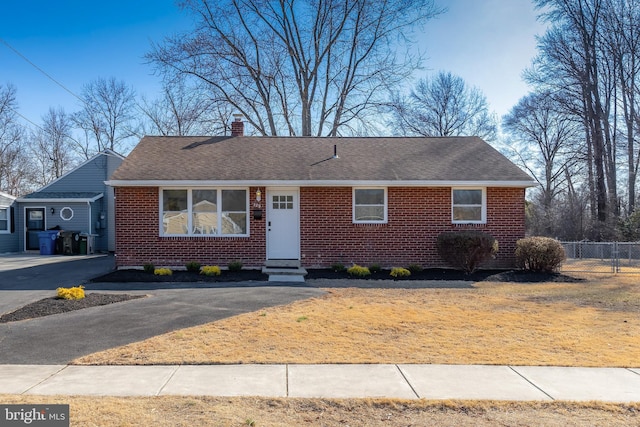 ranch-style house featuring entry steps, brick siding, a shingled roof, fence, and a chimney