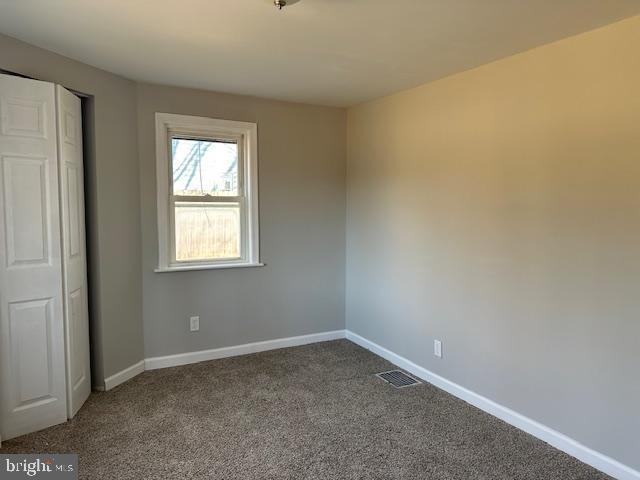 unfurnished bedroom featuring dark colored carpet, visible vents, and baseboards