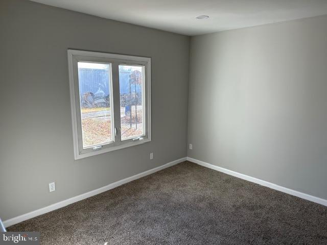 spare room featuring baseboards and dark carpet