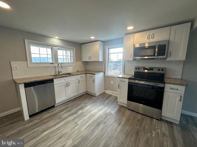 kitchen featuring baseboards, appliances with stainless steel finishes, wood finished floors, light stone countertops, and white cabinetry