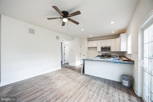 kitchen featuring visible vents, white cabinets, wood finished floors, stainless steel appliances, and a sink