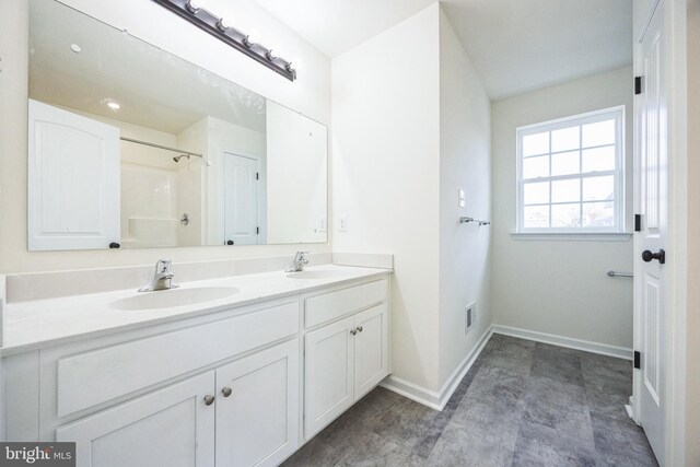 bathroom featuring a shower, a sink, baseboards, and double vanity