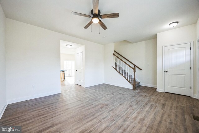 unfurnished living room with ceiling fan, stairway, wood finished floors, and baseboards