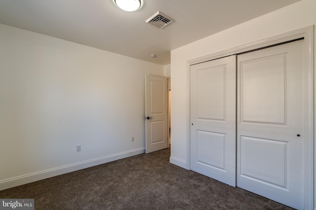 unfurnished bedroom with a closet, dark carpet, visible vents, and baseboards