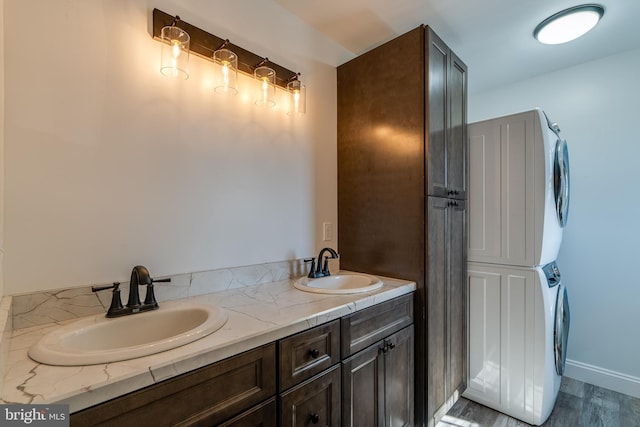 full bathroom featuring double vanity, a sink, stacked washer and clothes dryer, and baseboards