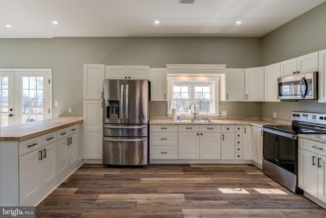 kitchen featuring stainless steel appliances, dark wood-type flooring, a peninsula, a sink, and white cabinets