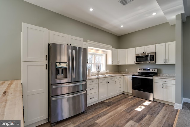 kitchen with dark wood-style flooring, visible vents, appliances with stainless steel finishes, white cabinets, and a sink