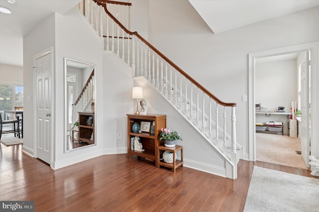 staircase featuring a towering ceiling, hardwood / wood-style flooring, and baseboards