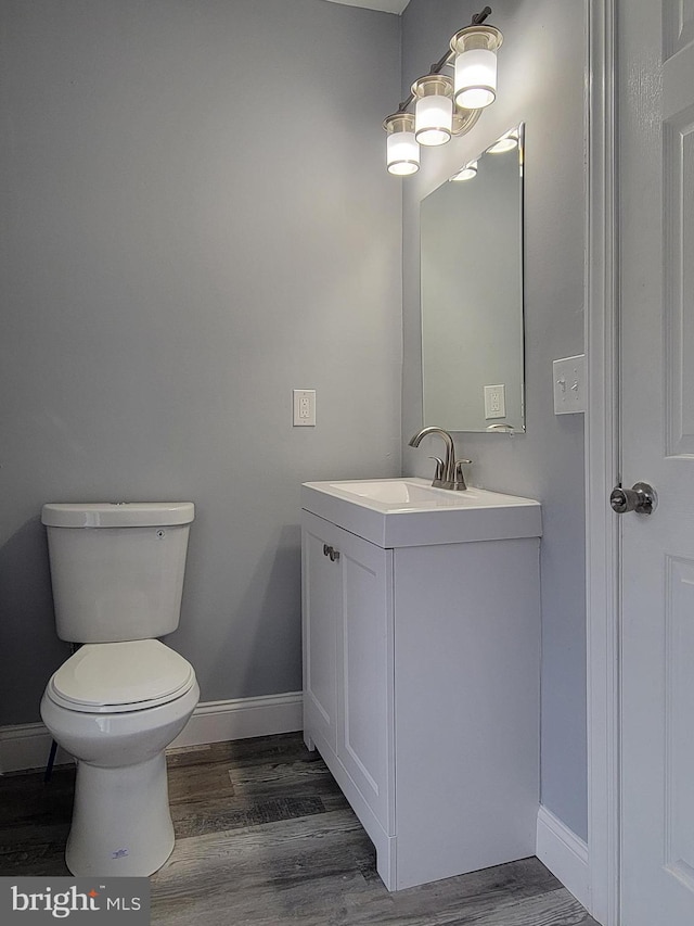 half bathroom featuring toilet, vanity, baseboards, and wood finished floors