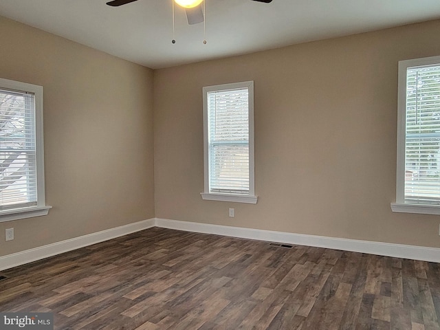 empty room featuring dark wood-style floors, a wealth of natural light, and baseboards