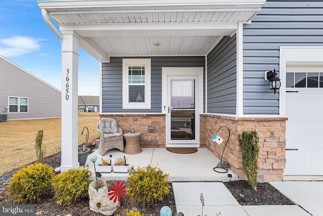 doorway to property with stone siding, a porch, and central AC