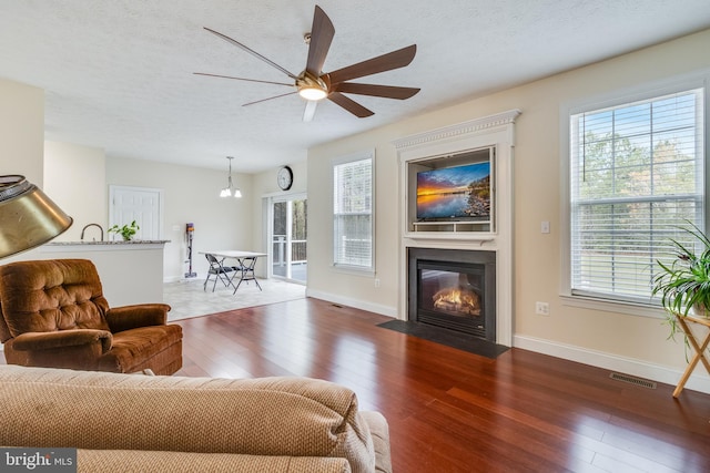 living room featuring a textured ceiling, hardwood / wood-style floors, a fireplace with flush hearth, and visible vents