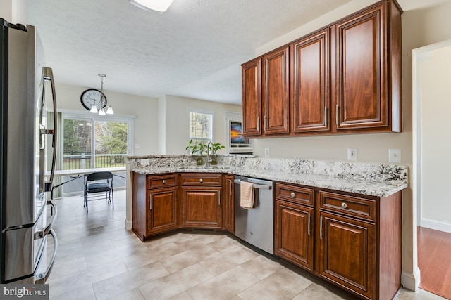 kitchen featuring appliances with stainless steel finishes, a sink, a peninsula, and light stone counters