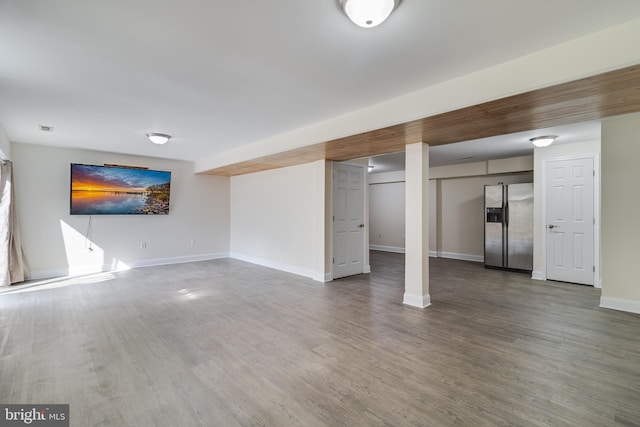 finished below grade area with visible vents, baseboards, wood finished floors, and stainless steel fridge with ice dispenser