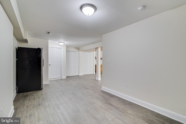 below grade area with visible vents, baseboards, wood finished floors, and freestanding refrigerator