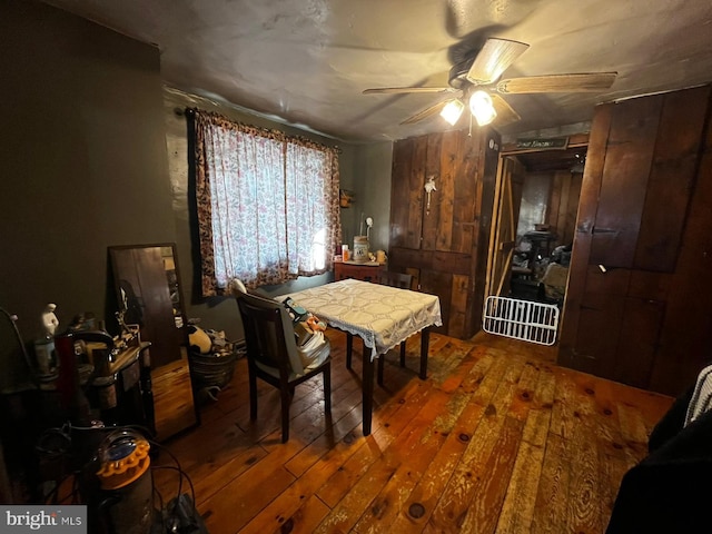 dining area featuring wood-type flooring, a ceiling fan, and wooden walls