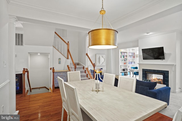 dining space featuring visible vents, stairway, ornamental molding, wood finished floors, and a fireplace