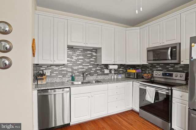 kitchen featuring decorative backsplash, light wood-style flooring, stainless steel appliances, white cabinetry, and a sink