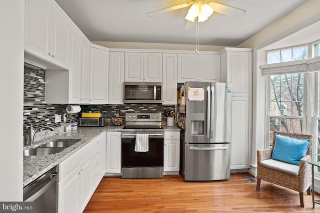 kitchen featuring tasteful backsplash, white cabinets, appliances with stainless steel finishes, light wood-style floors, and a sink