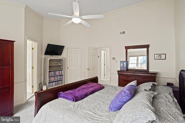 bedroom featuring ceiling fan, light carpet, visible vents, a towering ceiling, and crown molding