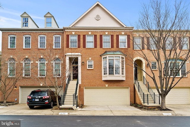 townhome / multi-family property with a garage, concrete driveway, brick siding, and stairs