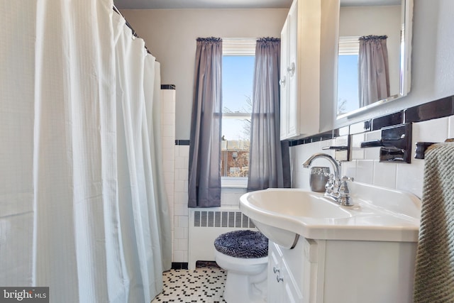 bathroom with tile walls, a shower with shower curtain, toilet, radiator heating unit, and vanity