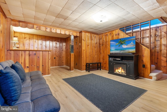 living area featuring wooden walls, a glass covered fireplace, stairway, and wood finished floors