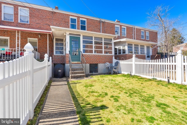 back of house featuring entry steps, fence private yard, brick siding, a sunroom, and a lawn