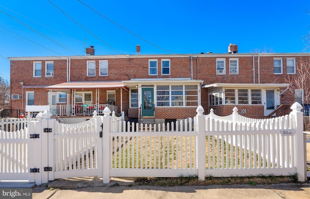 view of property featuring a fenced front yard, brick siding, covered porch, a gate, and a sunroom