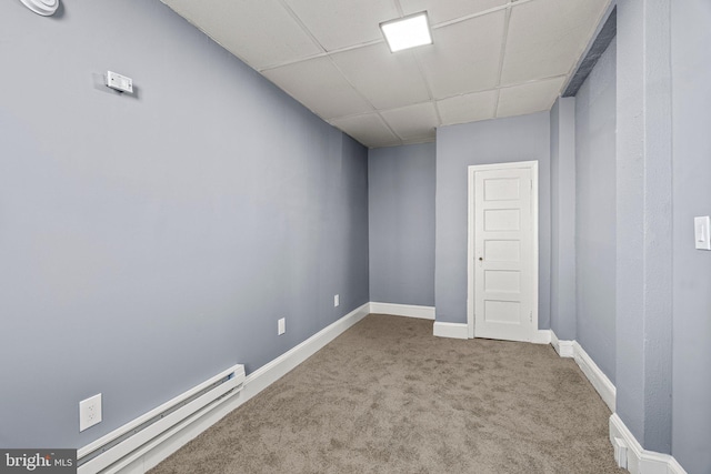 empty room with a baseboard heating unit, a drop ceiling, carpet floors, and baseboards