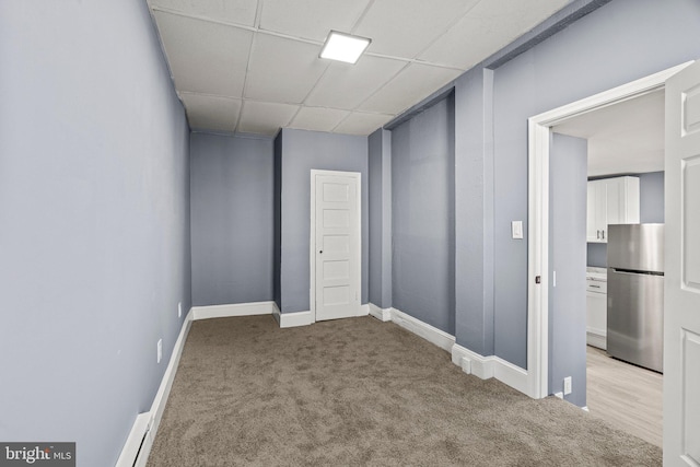 unfurnished room with baseboards, a drop ceiling, and light colored carpet