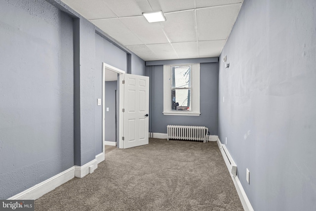 unfurnished room featuring carpet, radiator, a baseboard heating unit, a drop ceiling, and baseboards