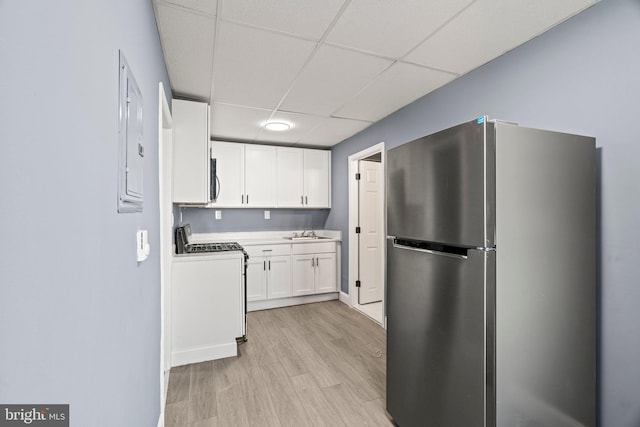 kitchen featuring light wood finished floors, white cabinets, appliances with stainless steel finishes, a paneled ceiling, and a sink