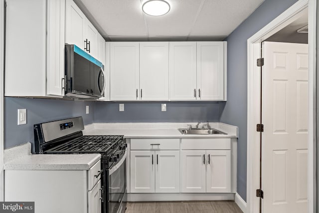 kitchen with light wood-style flooring, a sink, white cabinets, light countertops, and stainless steel gas stove