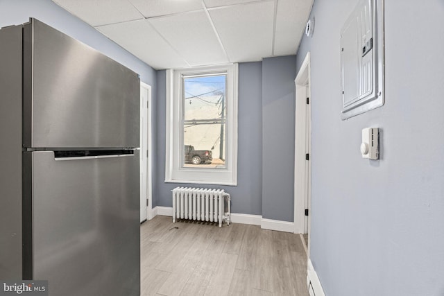 hallway featuring radiator heating unit, a drop ceiling, light wood-style flooring, and baseboards