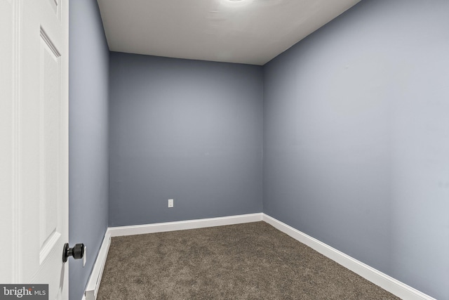 unfurnished room with baseboards and dark carpet