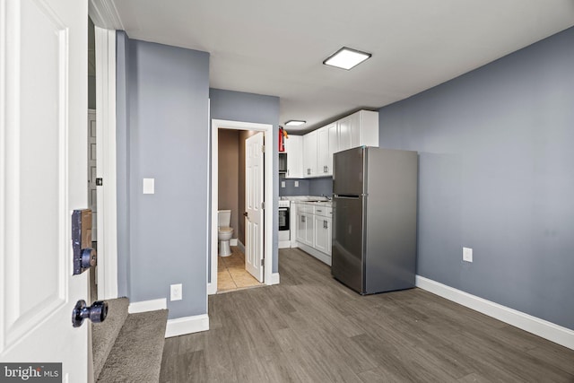 kitchen with baseboards, white cabinets, wood finished floors, freestanding refrigerator, and light countertops