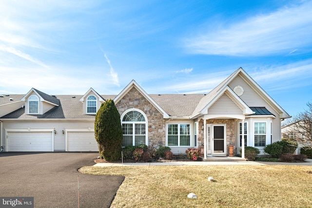 view of front of property featuring driveway, a garage, a shingled roof, stone siding, and a front lawn