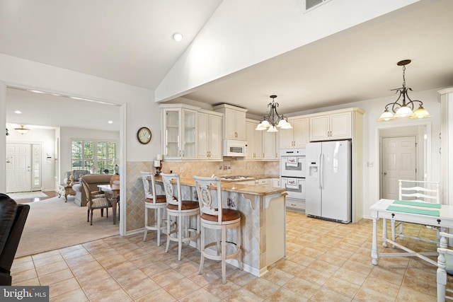 kitchen featuring glass insert cabinets, vaulted ceiling, white appliances, a peninsula, and a kitchen bar