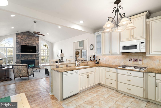 kitchen featuring open floor plan, a sink, a stone fireplace, white appliances, and a peninsula